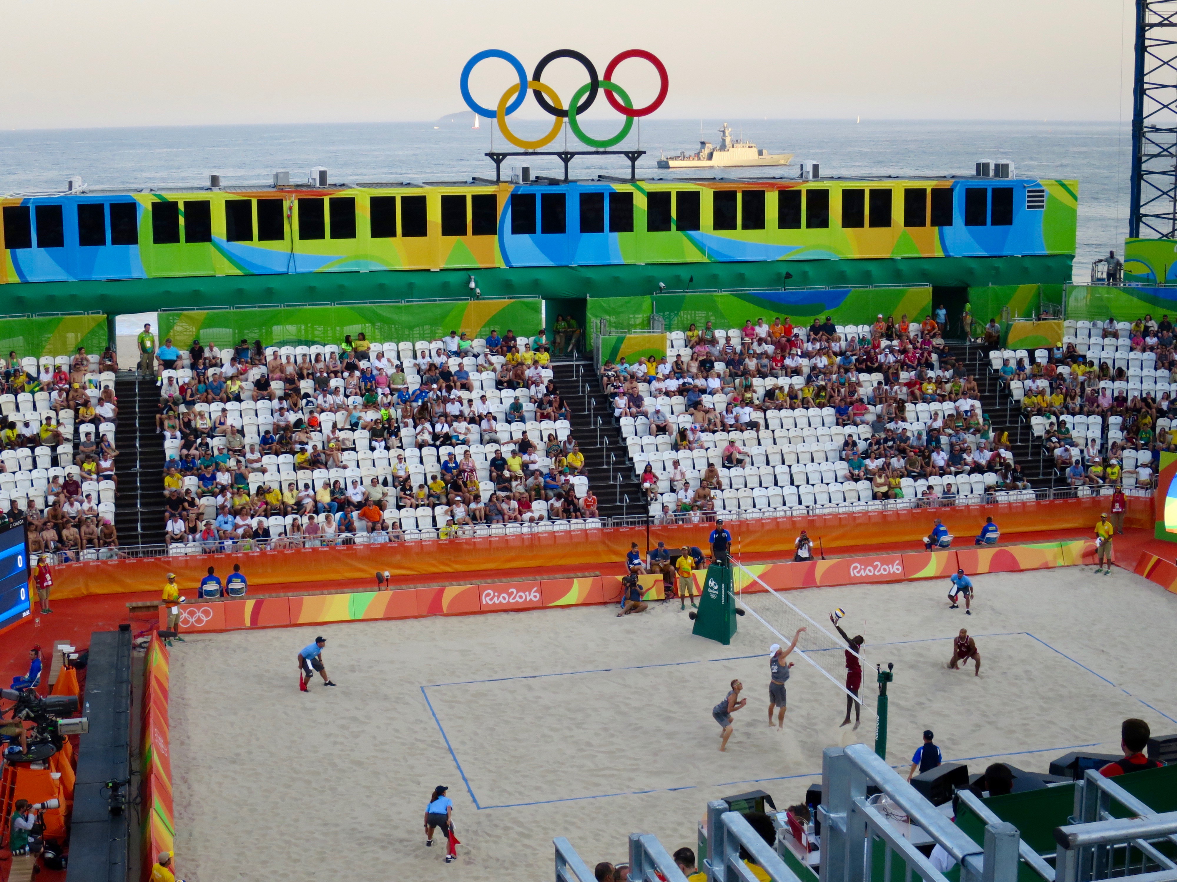 Beach Volleyball Arena - BVA on Copacabana Beach with a defender ship patrolling the area.